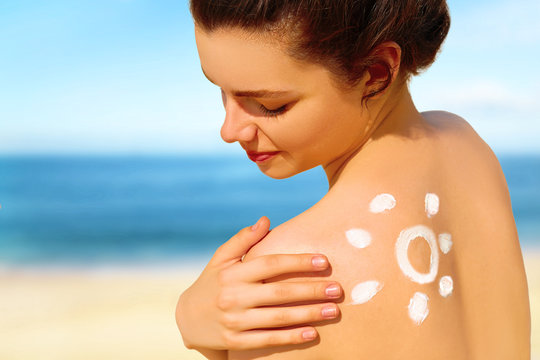 Portrait of gorgeous young woman smiling  in bikini with the drawn sun on a shoulder at beach