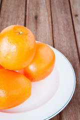 Orange on white plate put on wooden table.