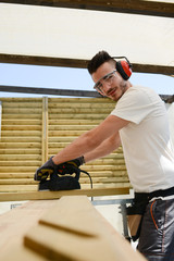 handsome young man carpenter working with electric tool on wood timber in construction site