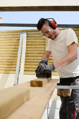 handsome young man carpenter working with electric tool on wood timber in construction site