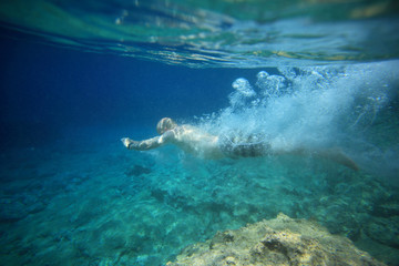underwater view of man diving in crystal clear coastal waters and landscape