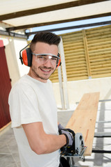 handsome young man carpenter working with electric tool on wood timber in construction site