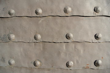 Old grey iron surface with rivets; rough, rusty texture; iron gate.