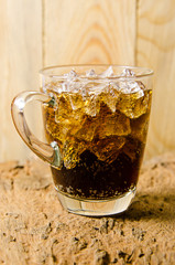 glass of cola with ice cubes on wooden background