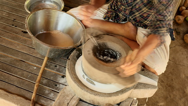 Woman sat cross-legged using hand-turned millstone to grind wet rice for making soaked rice flour