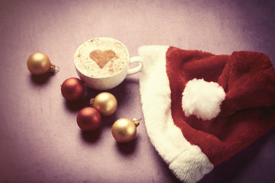 Cup of coffee with heart shape near Santas hat