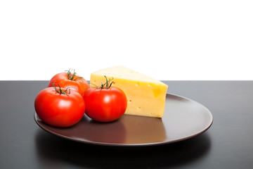Piece of cheese and tomatoes lying on the plate.