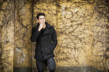 Handsome young man standing against plant covered wall