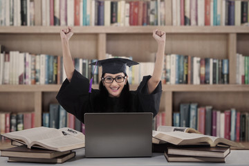 Successful female graduate with laptop at library