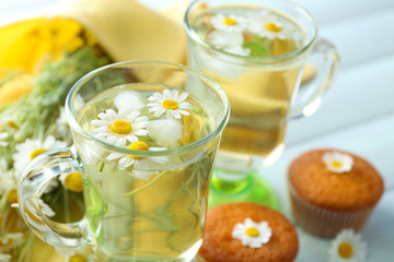 Cup of chamomile tea with chamomile flowers and tasty muffins on color wooden background