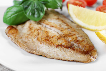 Dish of fish fillet with basil and lemon on plate close up