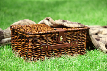 Obraz premium Wicker picnic basket and plaid on green grass, outdoors
