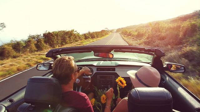 Happy Young Hipster Couple Driving Convertible on Country Road into Sunset. Romantic Freedom Vacation Concept. 20s-30s.