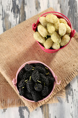 Ripe mulberries in buckets on table close up