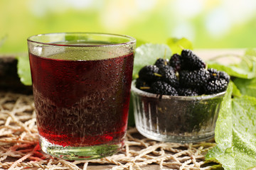 Glass of refreshing mulberry juice with berries on bright background