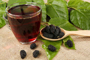 Glass of refreshing mulberry juice with berries on table close up