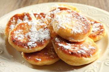 Fritters of cottage cheese in plate on wooden table, closeup