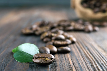 Coffee beans with leaf on wooden table close up