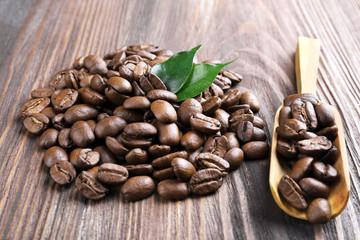 Coffee beans with leaves and spoon on wooden table close up
