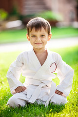 Smiling little boy in kimono sitting on grass in park