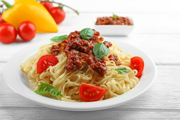 Spaghetti Bolognese on white plate, on color wooden background