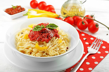 Spaghetti with tomato sauce and cheese on white plate, on color wooden background