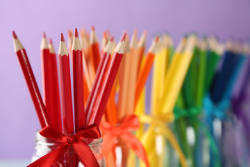 Bright pencils in glass jars on purple background