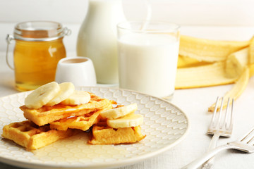 Sweet homemade waffles with sliced banana on plate, on light background