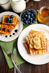 Sweet homemade waffles with sliced banana on plate, on light background