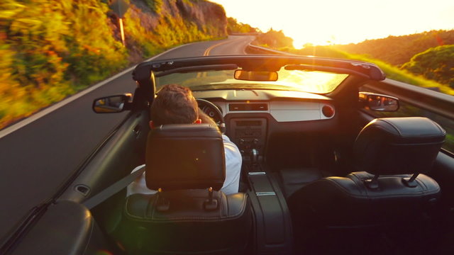 Happy Handsome Young Man Driving Convertible on Country Road at Sunrise. Steadicam Shot with Sun Flare. Freedom Travel Vacation Concept.
