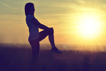 Silhouette of young woman stretching on a meadow at sunset