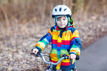 Fototapeta na wymiar kid boy in safety helmet and colorful raincoat riding bike, outd