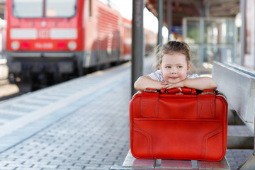 Cute little girl with big red suitcase on a railway station