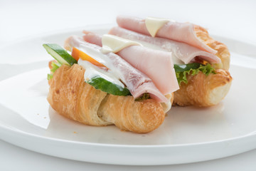 Croissant ham cheese sandwich on white plate