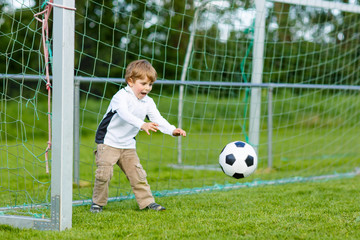 Two little sibling boys playing soccer and football on field