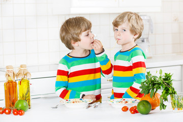 Two little kid boys eating spaghetti in domestic kitchen.