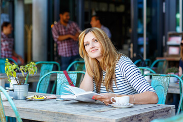 Woman drinking coffee and reading book in cafe