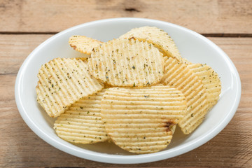 Potato chips in a white plate on wood background.