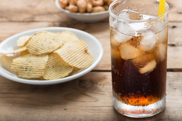 Cola glass with potato chips on a wood background.