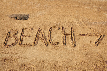 The word Beach with an arrow written in the sand on the beach