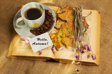 The cup of coffee lying ot the book with maple leaves