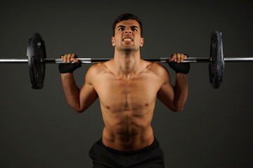 Fototapeta na wymiar Athlete young man exercises with dumbbell on gray background
