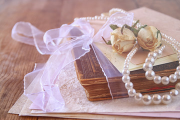 selective focus image of dry roses, white pearls necklace and old vintage books 