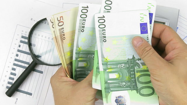 Businessman believes euros and throws them at documents, 
calculator, magnifying glass