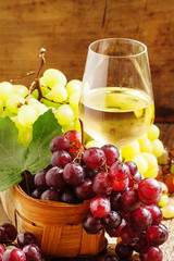 White wine in a glass and green and red grapes in a wicker baske