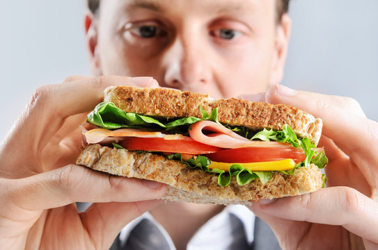 Close up of a business man eating a healthy ham, cheese, tomato sandwich, selective focus on food