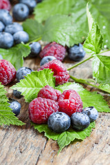 raspberries and blueberries with leaves on the old wooden backgr