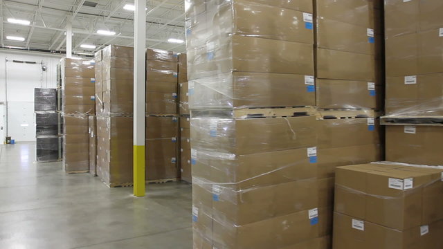 Tracking shot, moving through a factory warehouse with stacks of boxes.
