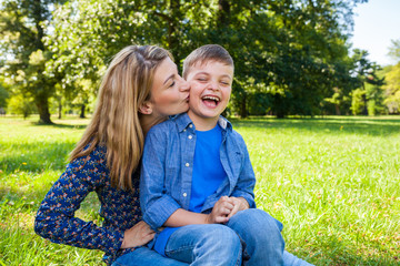 Fototapeta premium mother kissing her laughing son in the park