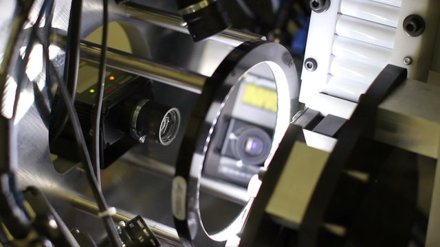 Tilting down, revealing 4 cameras inspecting every angle of products as they quickly pass through an automated system.
